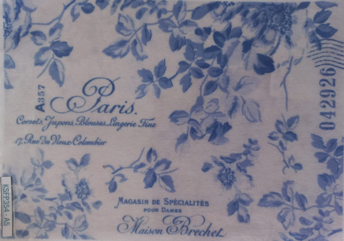 A square white fabric napkin or handkerchief with a blue floral toile pattern, featuring printed French text including 'Paris', 'Maison Dreyet', and a barcode on the left edge.
