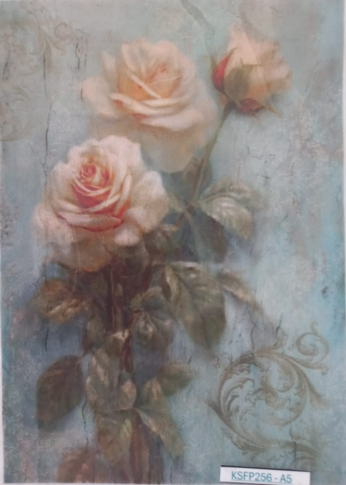 A vintage-style floral art print featuring three cream and pale pink roses with green leaves on a textured light blue background. The print has a distressed, aged aesthetic with a white border and a small label at the bottom right.