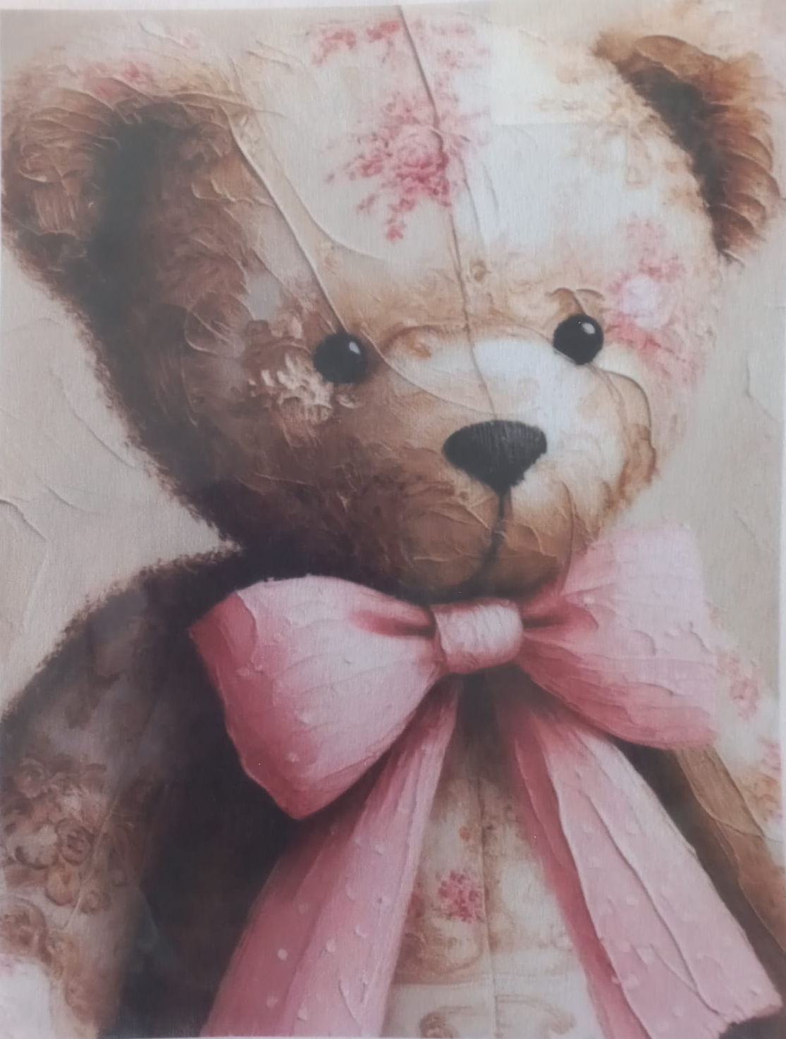 A close-up of a teddy bear illustration or print featuring a brown bear with a large pink bow, cream face, and soft pink floral details on a textured background.