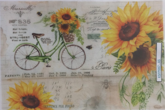 A square decorative paper or card featuring a vintage-style sunflower and bicycle collage, sealed in a clear plastic sleeve. The design includes large yellow sunflowers, a green bicycle with flowers, handwritten text, and old-fashioned print elements on a light beige background.