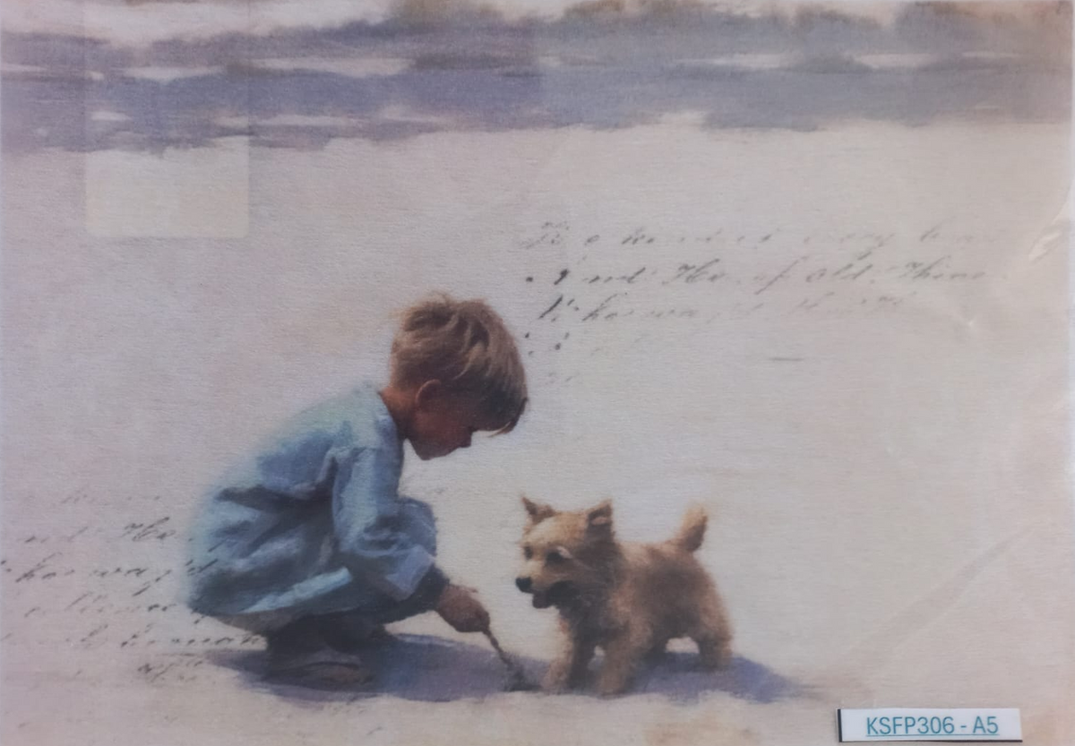 A vintage-style art print or postcard depicting a young boy in a blue shirt crouching beside a small brown dog on a pale beach or snowy ground, with faint handwritten script in the background. The print is photographed flat against a white surface with a protective sleeve visible around the edges.