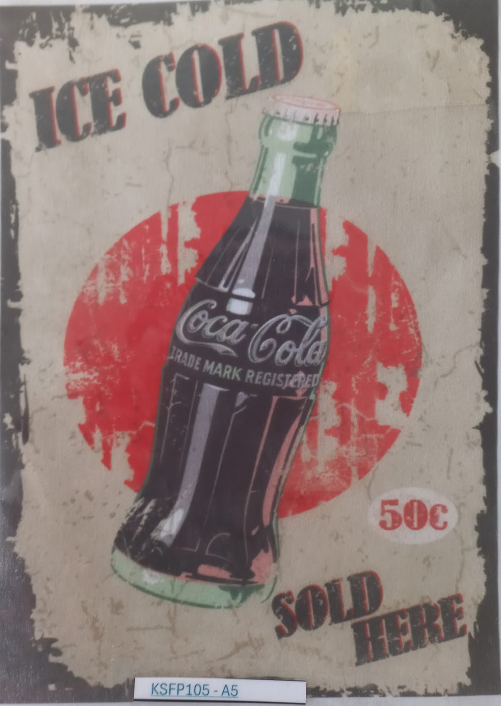 A vintage-style Coca-Cola advertising print or poster showing an ice-cold glass bottle with a red circular background and distressed text reading 'ICE COLD' and 'SOLD HERE'. The print is photographed inside a clear protective sleeve on a white background.