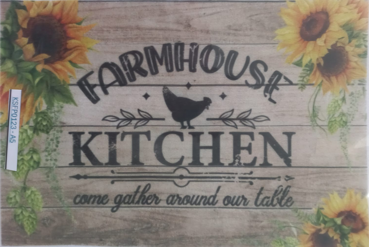 A square decorative sign or print with a rustic wood-plank background, featuring the words “FARMHOUSE KITCHEN” in dark lettering, a black chicken silhouette, sunflower illustrations in the corners, and the phrase “ome gather around our table” near the bottom. The item appears to be photographed inside a clear plastic sleeve, with a small white label visible on the left edge.