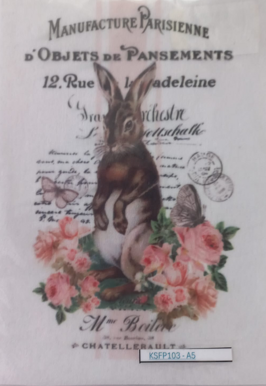 A vintage-style printed card or label inside a clear protective sleeve, featuring a rabbit among pink roses with French text including 'Manufacture Parisienne d'Objets de Pansements' and a small label at the bottom reading 'KSFP103-A5'.