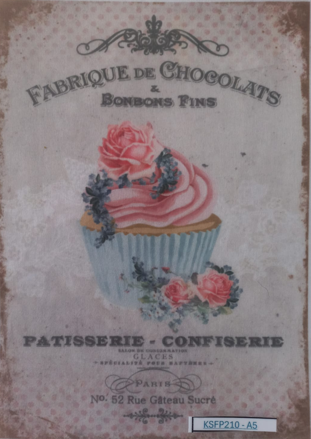 A vintage-style chocolate and pastry label or print featuring an illustrated pink frosted cupcake with roses, surrounded by decorative text including 'Fabrique de Chocolats & Bonbons Fins' and 'Patisserie - Confiserie'. The print is photographed inside a clear plastic sleeve on a white background.