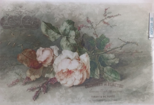 A vintage-style floral print or label featuring pale pink roses, green leaves, and muted botanical text on a soft gray-green background, photographed inside a clear plastic sleeve.