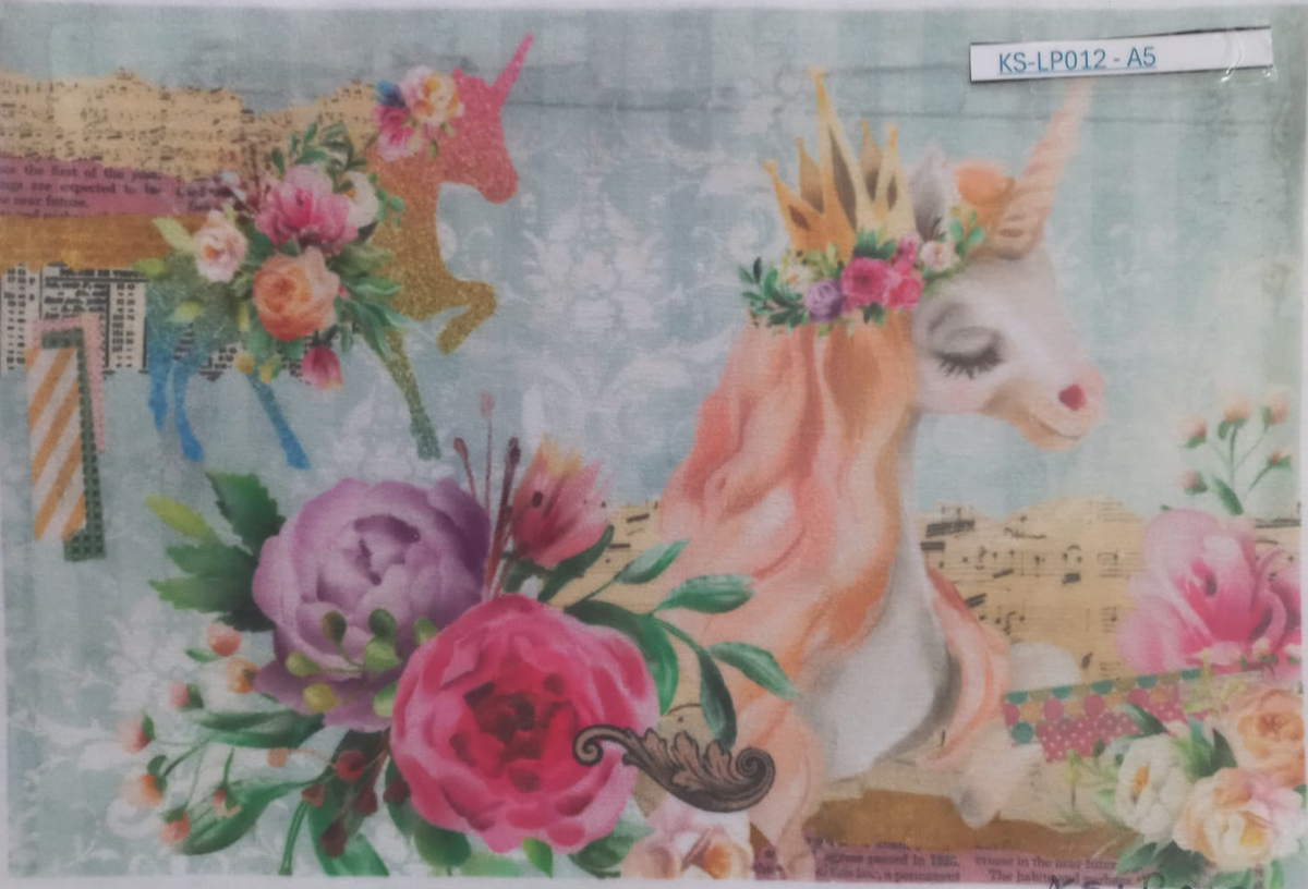 A rectangular printed card or art piece featuring a whimsical unicorn collage design, photographed inside a clear plastic sleeve. The artwork shows a white unicorn with closed eyes, a gold crown, a floral crown, and a pink horn, surrounded by large pink and purple flowers, green leaves, and musical notes on a pale blue patterned background.